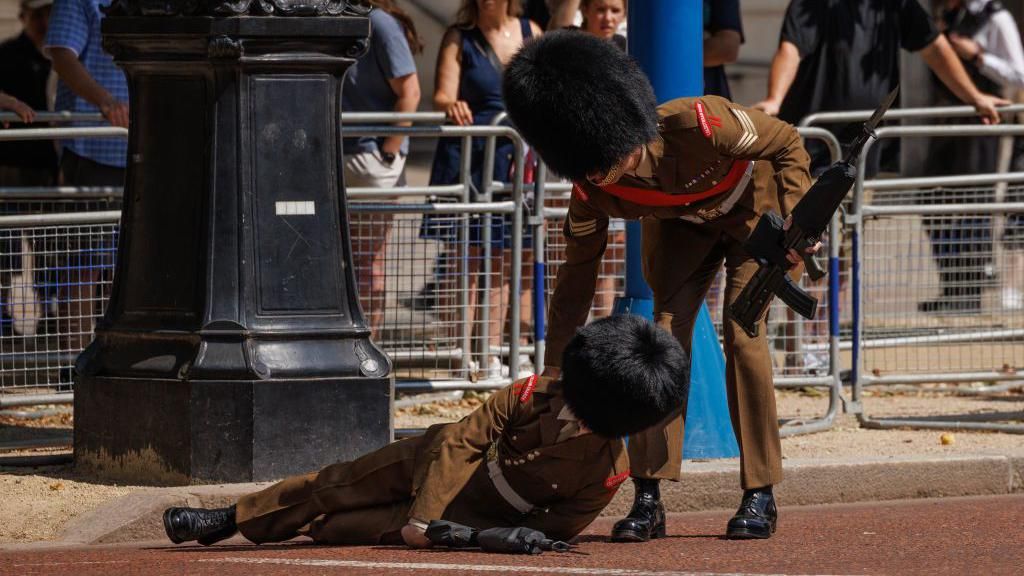 A foot guard is lifted up by another member of the Army after he fainted on the Mall