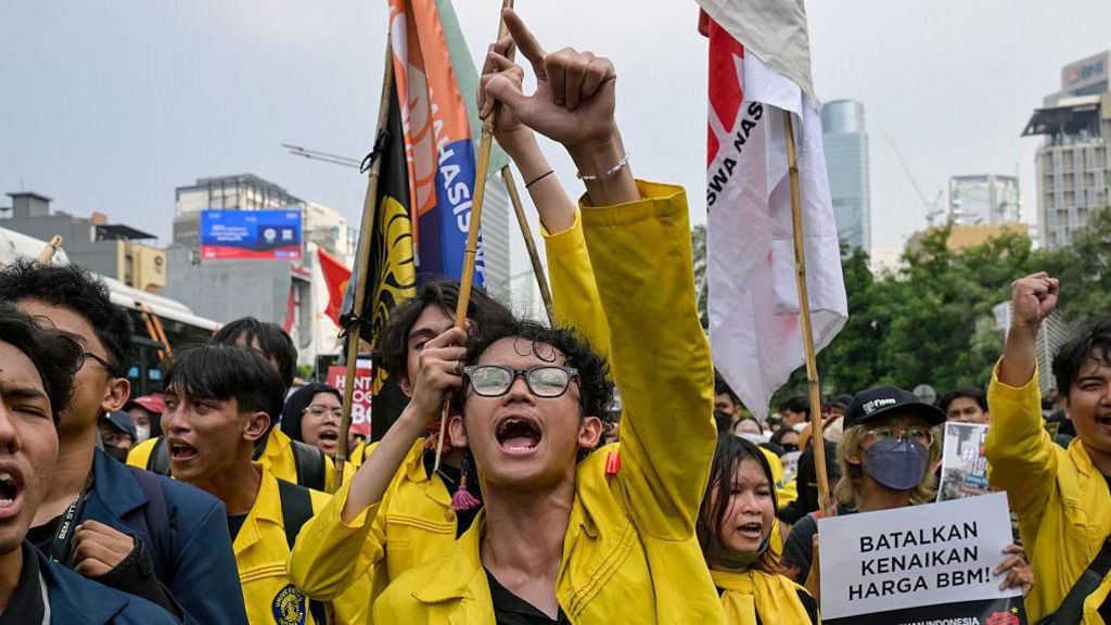 An Indonesian student protester wearing yellow marching on the street in Jakarta with one arm raised
