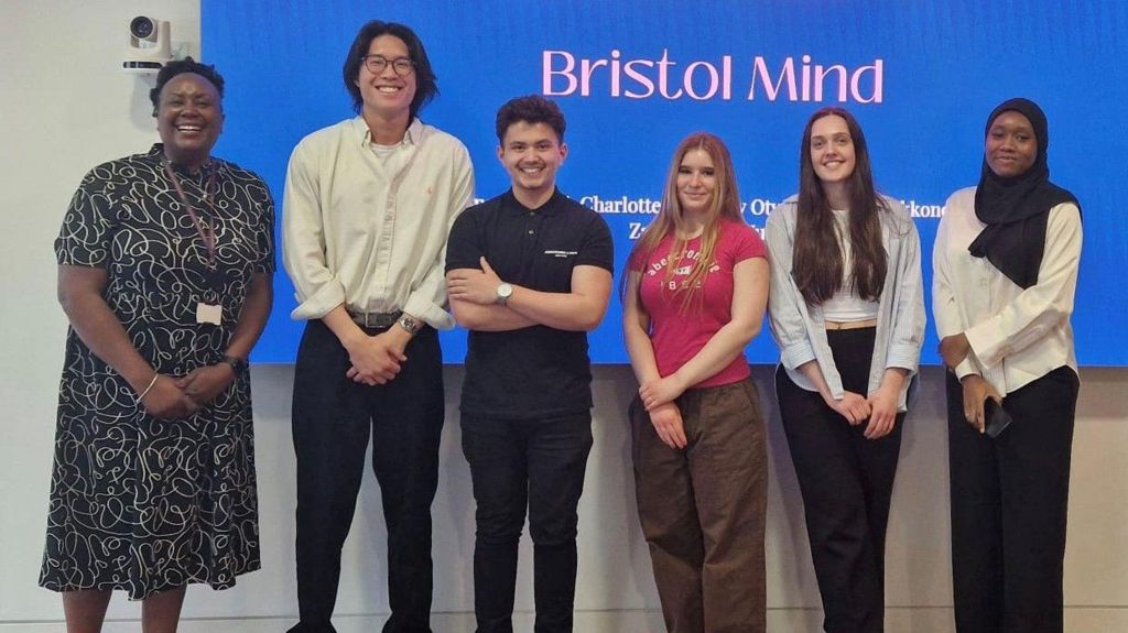 Bristol University students stand in front of the a white board with the words 'Bristol Mind' behind them