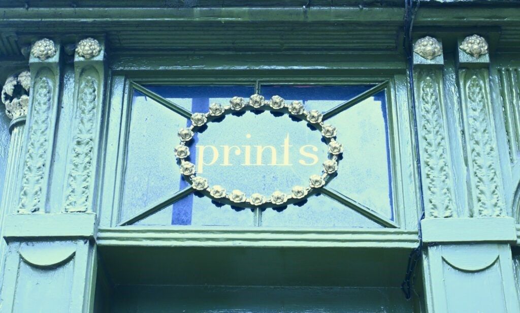 An ornate blue window sign that says 'prints' 