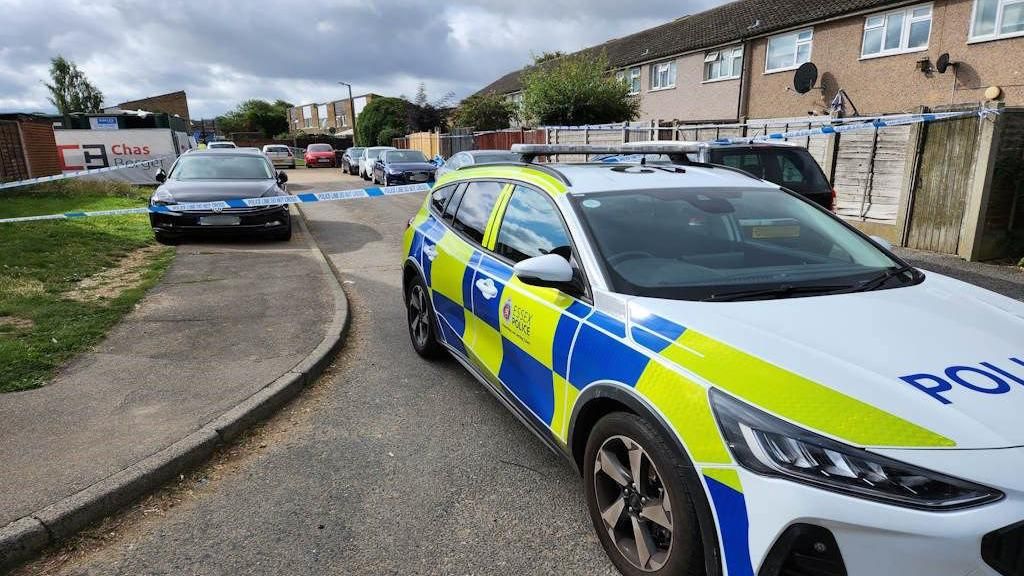 A police car in front of a cordoned off area on a housing estate