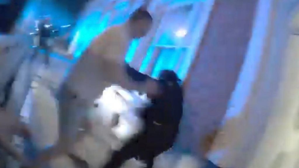 A grainy still from footage of a police officer being attacked by a man in a white T-shirt in the street.