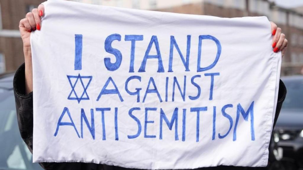 A member of the public holds up a sign with the words 'I stand against antisemitism'