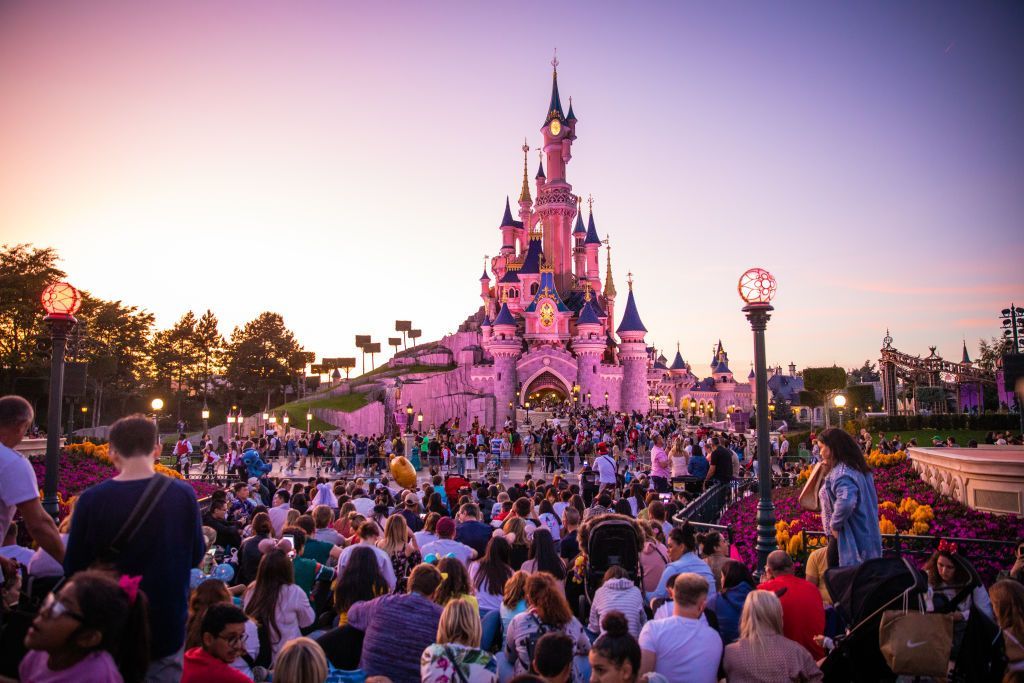 A view of the Sleeping Beauty Castle during the sunset at Disneyland Paris, in Paris, France - crowds gather in front of the castle and the sky and castle are tainted pink.