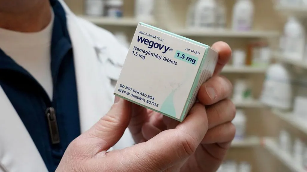 A close-up of a pharmacist holding a box of Wegovy weight-loss pills in a pharmacy