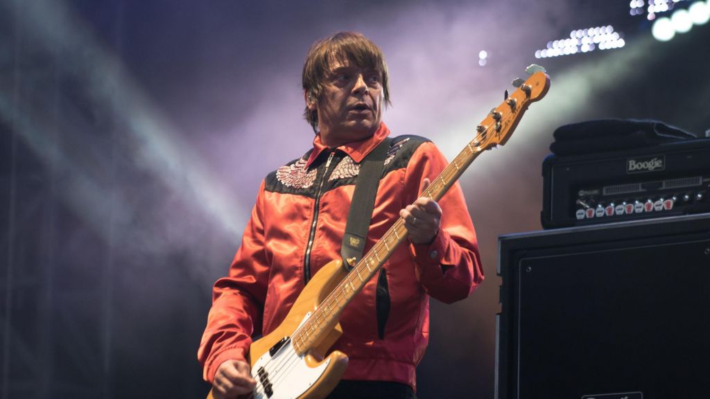 Mani playing bass on stage, wearing a red jacket