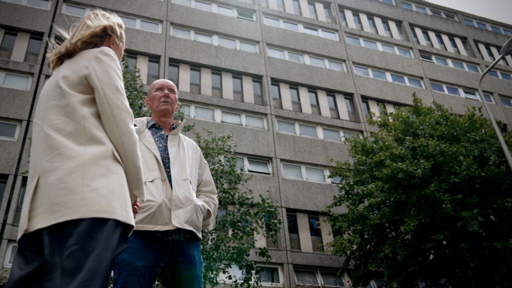 Katie Razzall with blond hair, white jacket and trousers talking to Irvine Welsh, bald, in white anorak and jeans outside the Banana flats in Leith