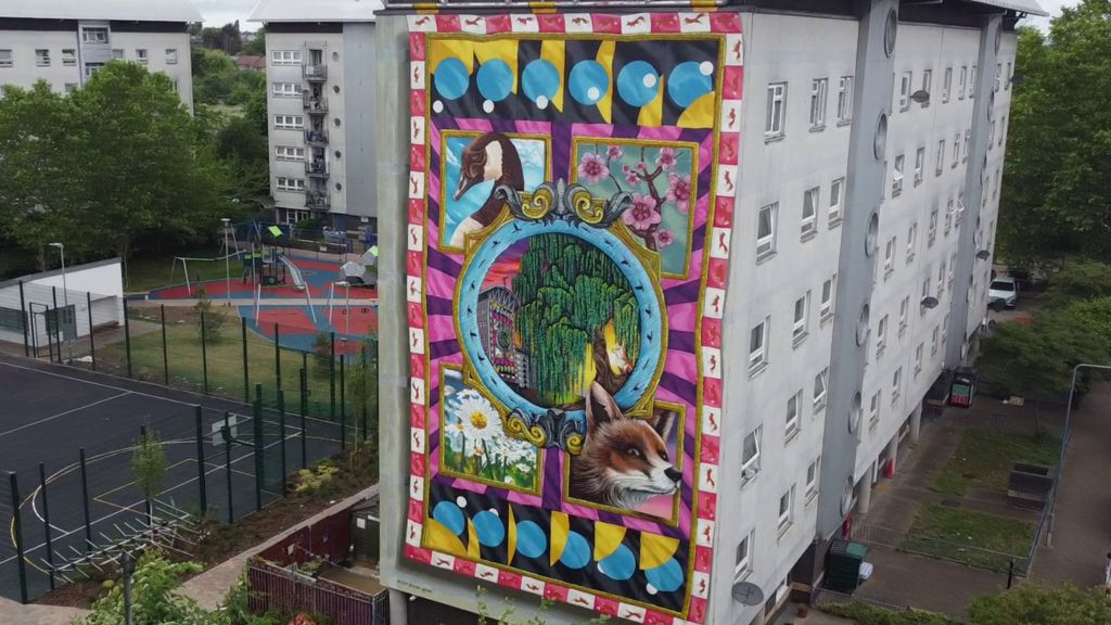 A white block of flats with a large mural draped down one side 