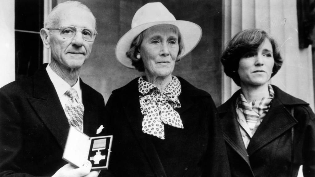 Archive image showing Nairac's family, father Maurice with short grey hair and glasses, mother Barbara with white hat and scarf and sister Rosamonde with short dark hair and dark jacket