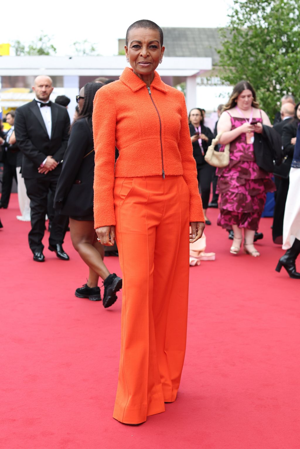 Adjoa Andoh in bright orange trousers and a matching zip-up top
