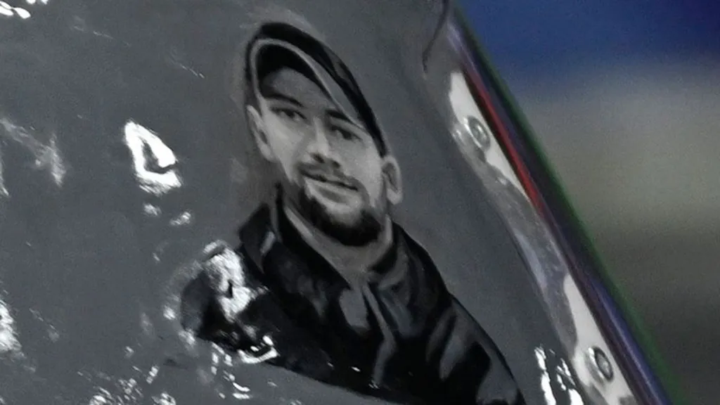 Close up of the helmet featuring an illustration of Taras Shpuk, who is bearded and is wearing a black cap and jacket.