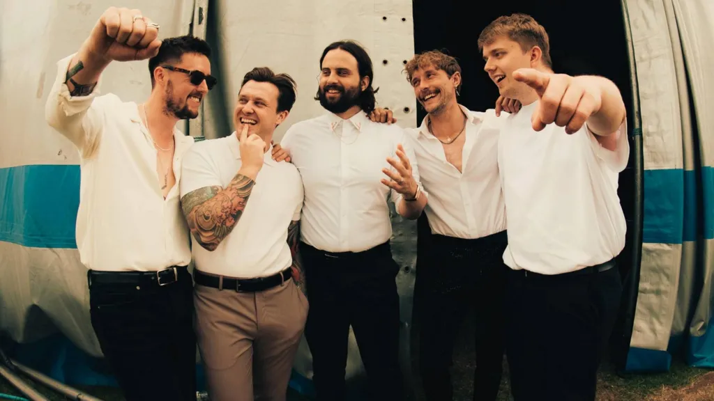 The band huddle outside a tent at a festival, all smiles.