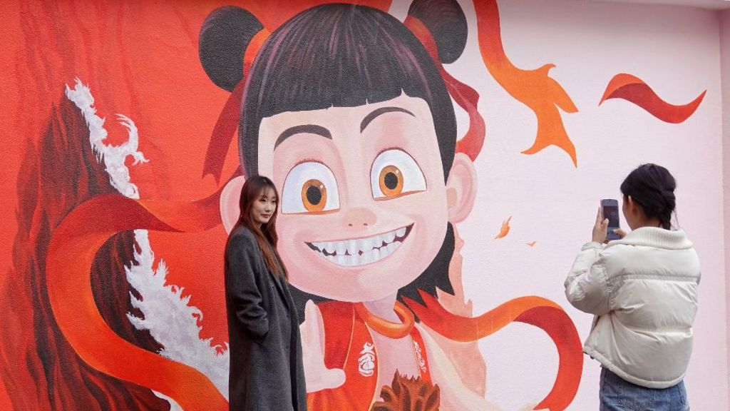 A woman takes photos in front of a Ne Zha themed wall painting on a street in Yantai, East China's Shandong province on 14 March, 2025