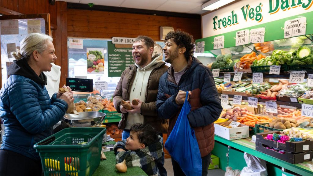 Two men and a young boy buying fruit and veg in a greengrocers.