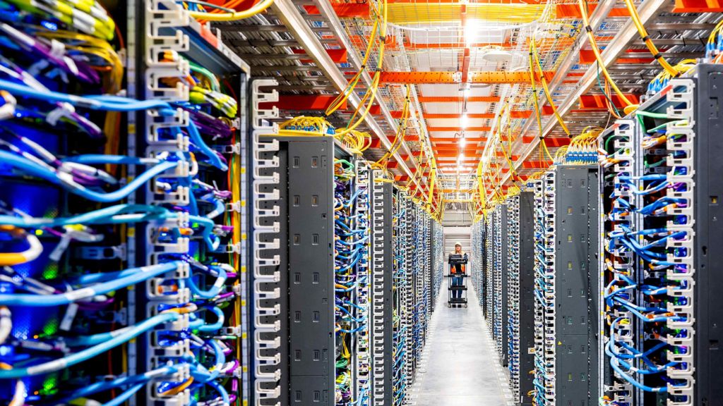 A technician pushing a cart walks through rows of wires inside a data centre.