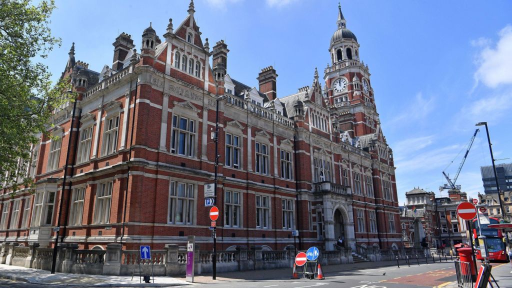 Croydon Town Hall taken from outside, a large red bricked building in the Victorian style with a clock tower and large stone archway entrance.