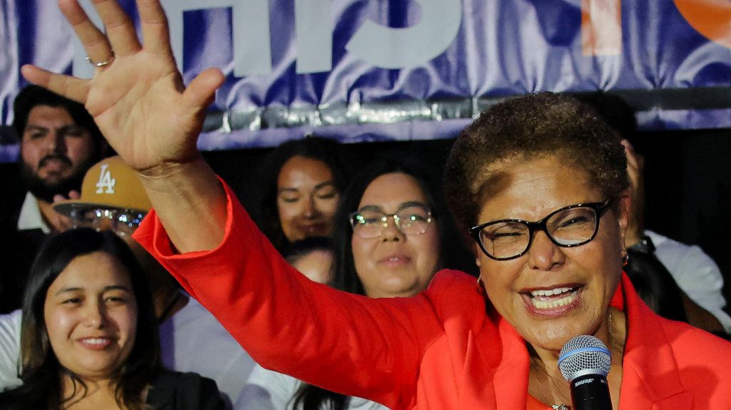 Incumbent mayor Karen Bass holds her hand up in a wave as she speaks at a microphone in front of supporters