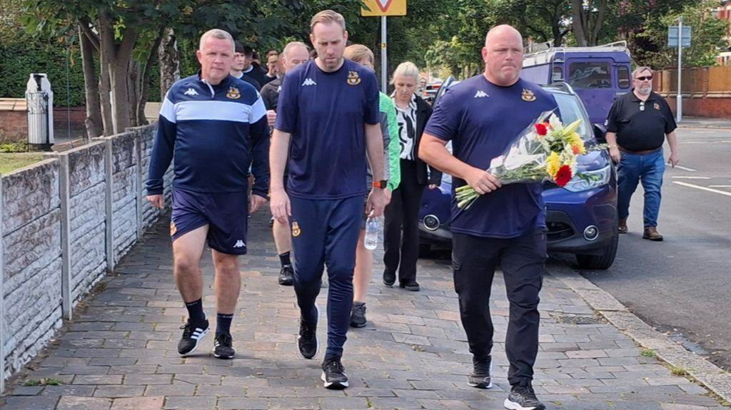 Southport manager Jim Bentley (right) and his players and staff walk from the club's Haig Avenue ground to place flowers at the police cordon in nearby Hart Street 