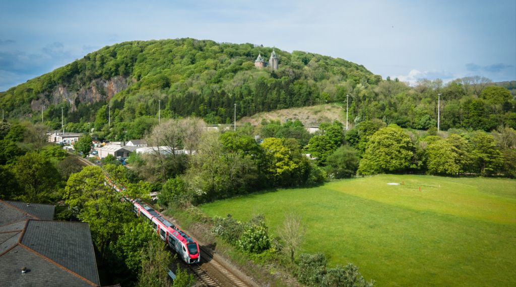 A train travels on a train track surrounded by fields and trees