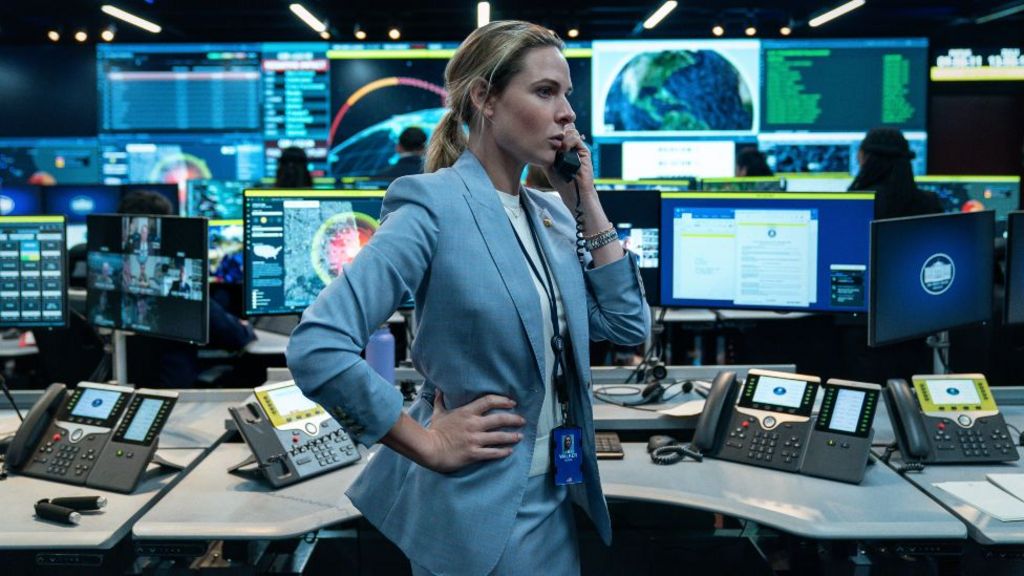 Rebecca Ferguson in A House of Dynamite, surrounded by screens, talking on the phone