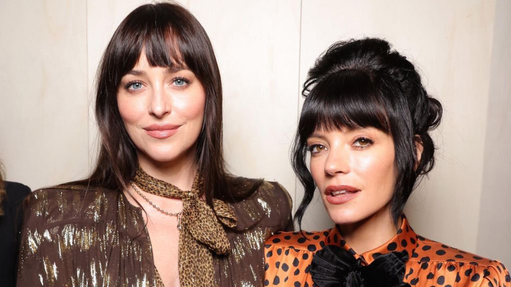 Dakota Johnson has her brown hair down and wears a leopard neck scarf and brown dress. Lily Allen has her black hair pinned up and is wearing an orange and black polkadot dress.