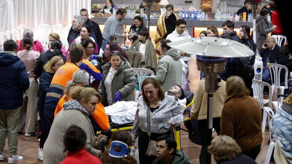 A patient in a hospital stretcher and dozens of others are draped in blankets, given water, and helped by medical workers at the Caseta Municipal.