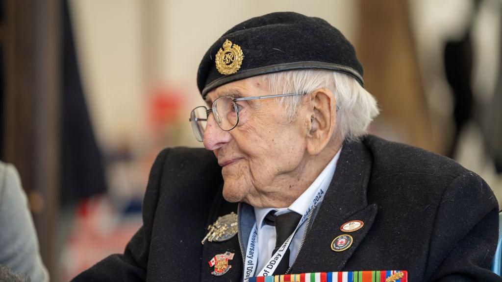 Don Sheppard, appearing with white hair, glasses, a dark-coloured suit and military medals