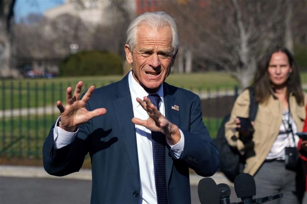 Peter Navarro, wearing a navy suit, is shown gesturing as he speaks to reporters outside the White House in March