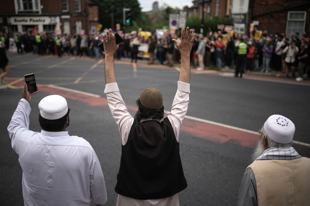 Three Muslum men gesture towards a crowd of anti-racism protesters in Sheffield on 7 August