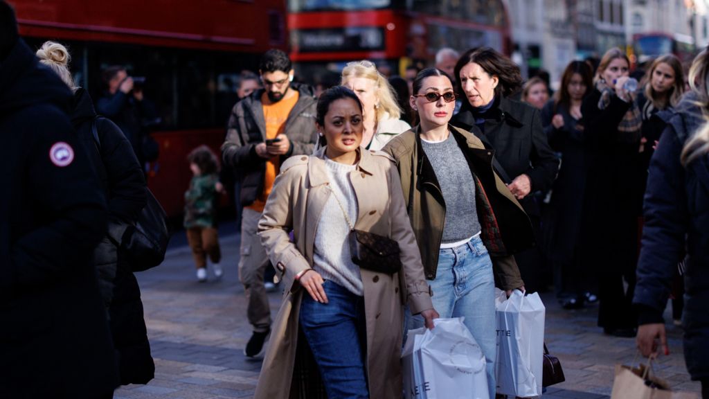 A crowd of shoppers walk down Oxford Street, some are carrying shopping bags.