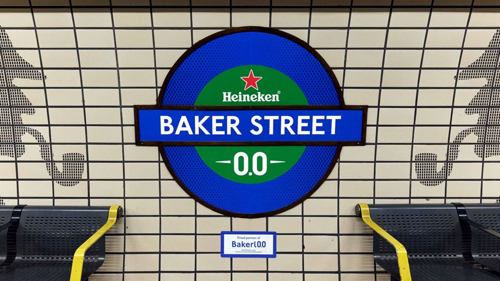 A London underground a wall sign reading “Baker Stret”, with Heineken branding inserted. The TFL sign is blue anbd green . Bakerloo is spelled with "0.0" instead of "oo" at the end