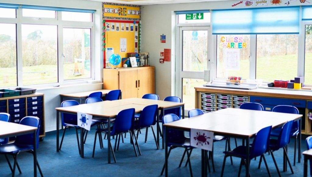 An empty classroom with blue plastic chairs around group tables