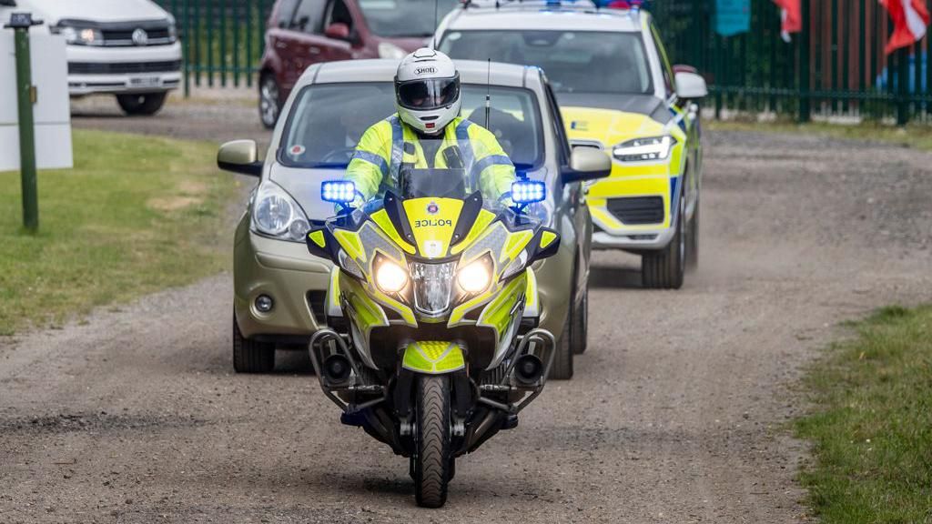An Essex Police motorbike rider, escorting a civilian car and another police car behind