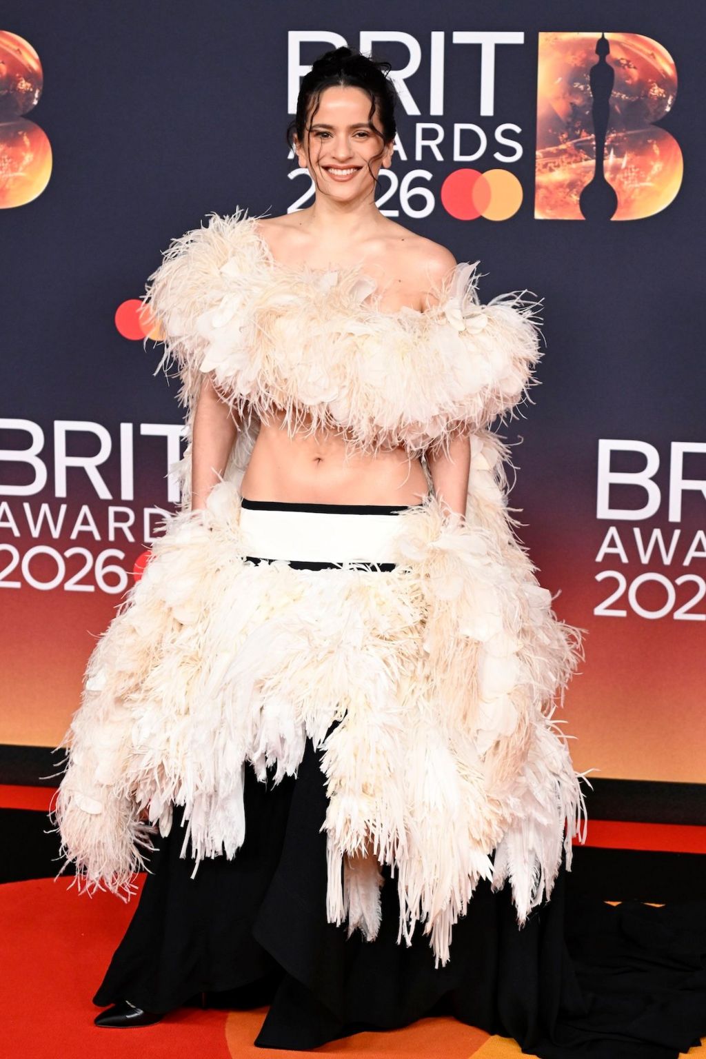 Rosalía wears a feather top and skirt with a white waistband
