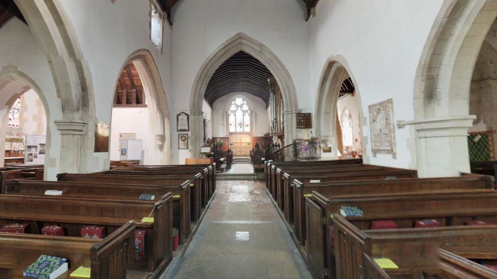 A google maps image of the interior of St Michael's Church Betchworth showing the aisle, rows of pews, pillars and traditional stained glass windows