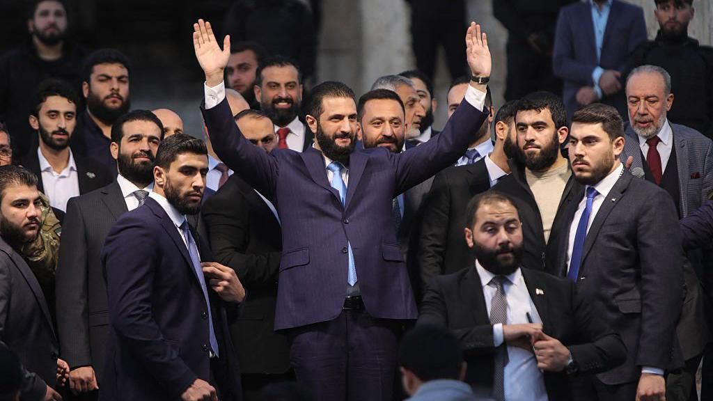 Ahmed al-Sharaa waves to the crowd at the gate of Aleppo's Citadel during celebrations marking one year since an Islamist alliance, led by Sharaa, entered the northern city and swiftly took control of it, on 29 November 2025.
