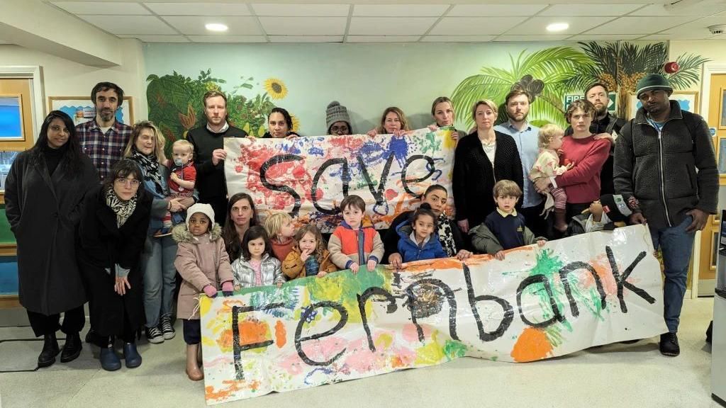 Save Hackney's Children's Centres campaign group members holding two  banners, one which says Save on it, the other which says Fernbank on it.