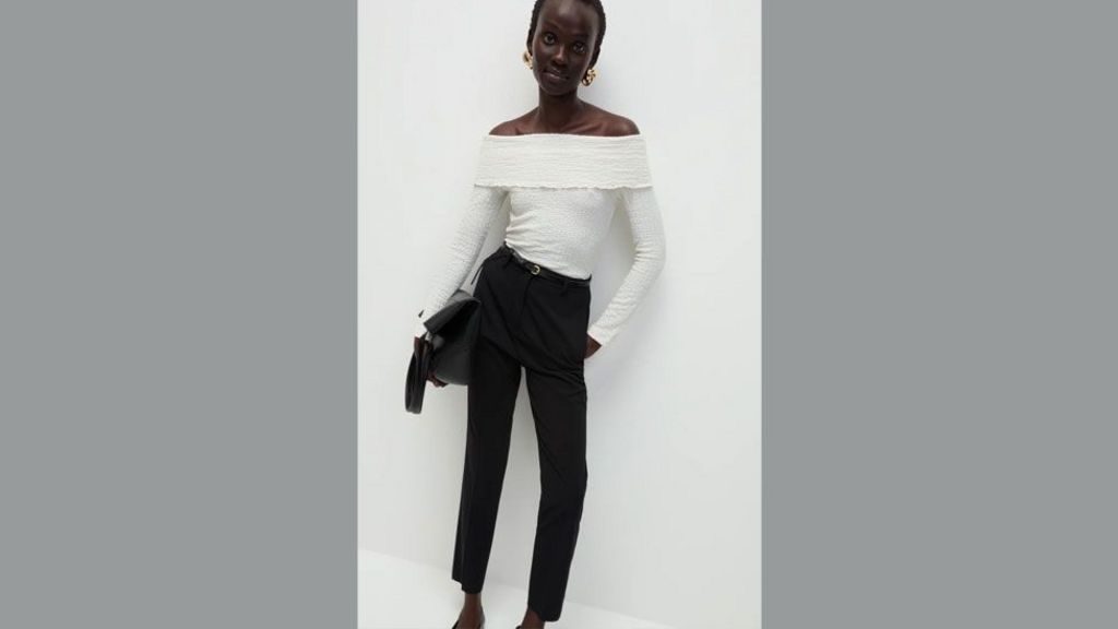 M&S model poses in white top and black trousers and leans against a white wall