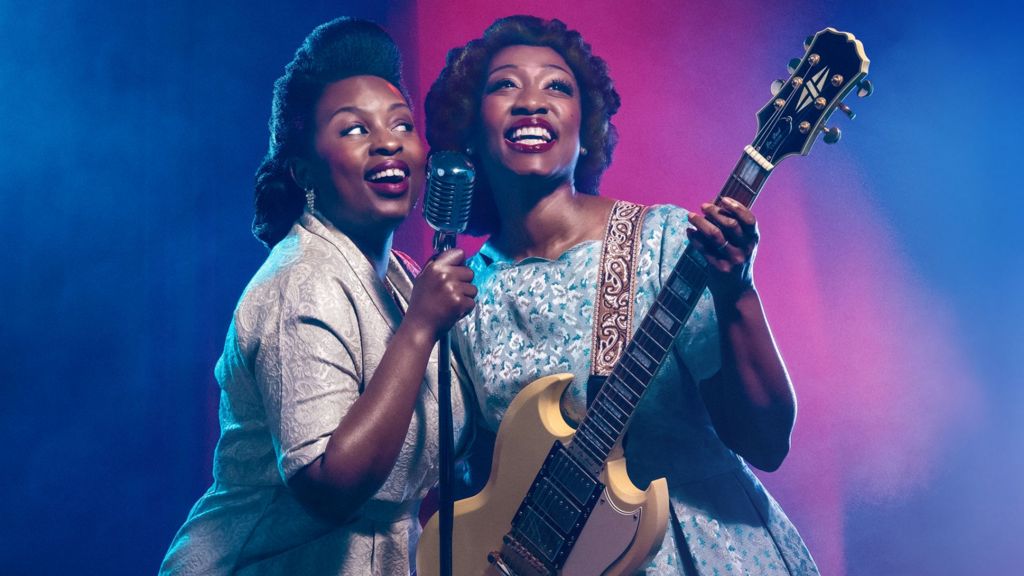 Artwork from the show Marie and Rosetta. The photo pictures two women dressed in 1940s dresses. The woman on the left is holding a microphone and singing joyfully. The woman on the right, Beverley Knight is smiling and holding a guitar.