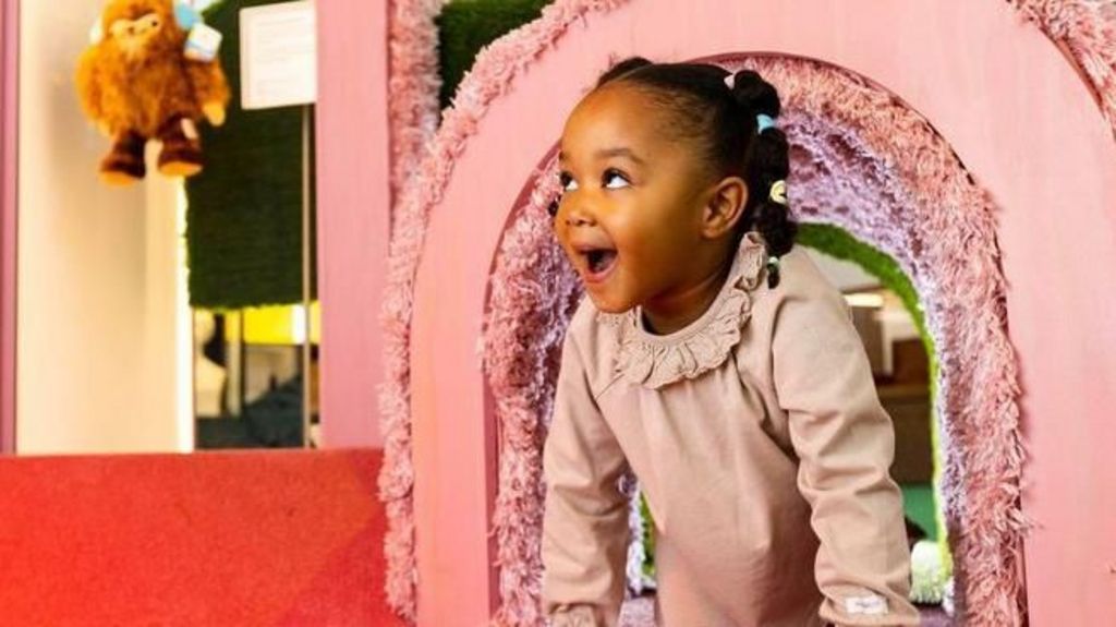 A young girl looks excited as she emerges from a pink rainbow installation at the museum