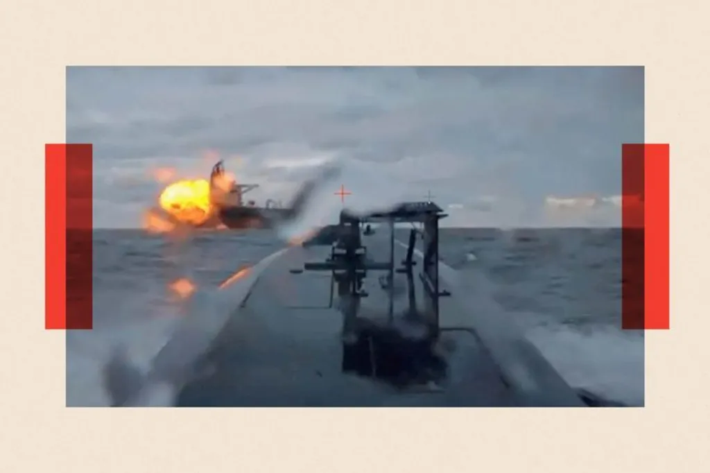 A blurry photograph showing a sea vessel in the distance being engulfed in flames. The photograph is taken from a sea drone