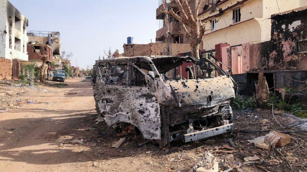 This picture taken on May 30, 2024, shows a burnt vehicle in front of damaged shop in Omdurman