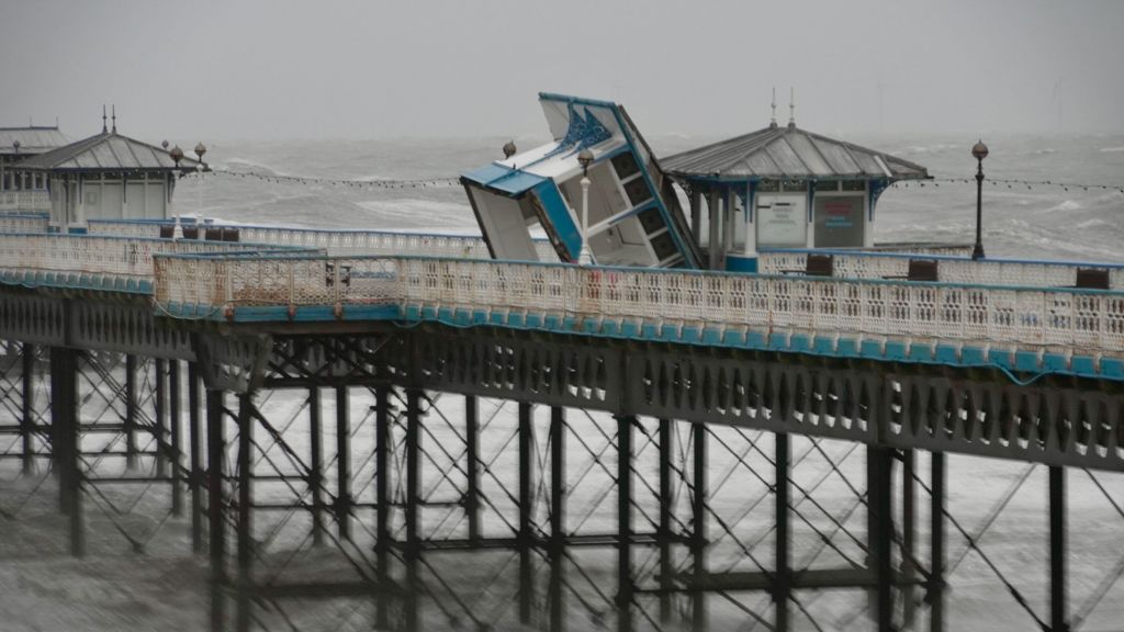 A white and blue wooden unit on Llandudno Pier appears on its side amid a gloomy and stormy backdrop