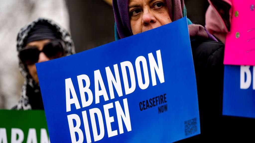 A woman holds up a sign reading "abandon Biden"