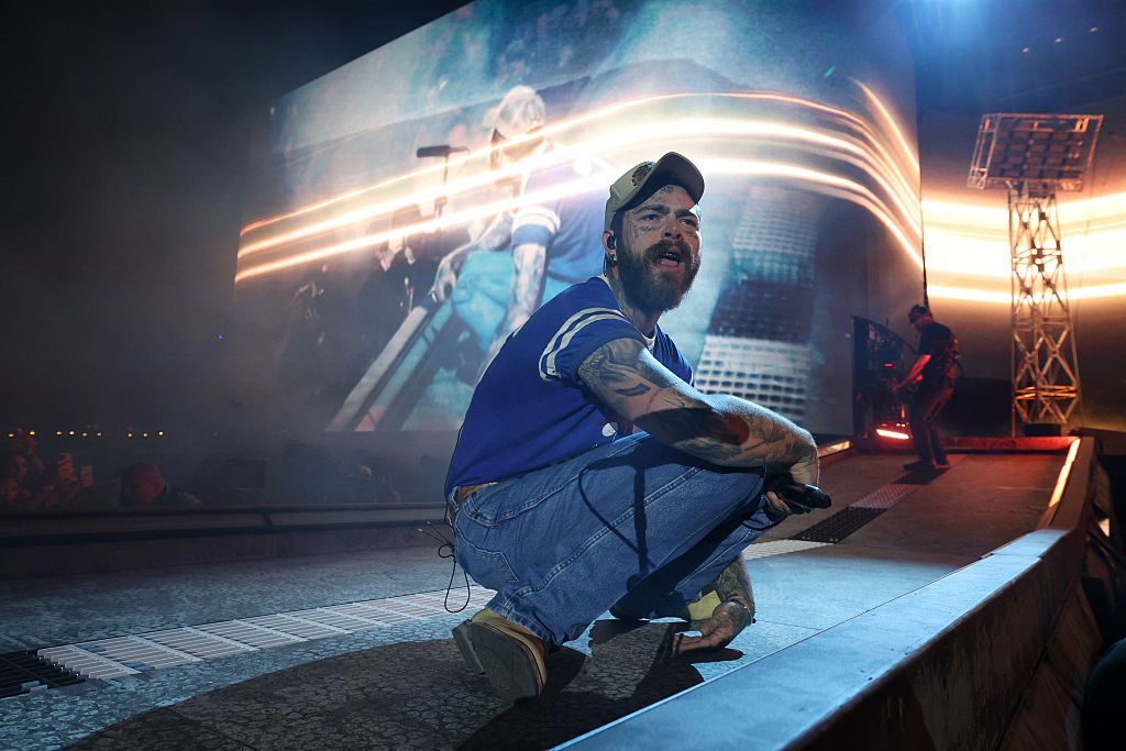 Post Malone crouches on a catwalk during his headline set at the Coachella Festival