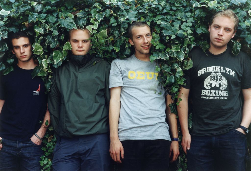 Coldplay in 2000 - the four band members stand leaning backwards into a hedge, with Chris Martin smiling at the camera 