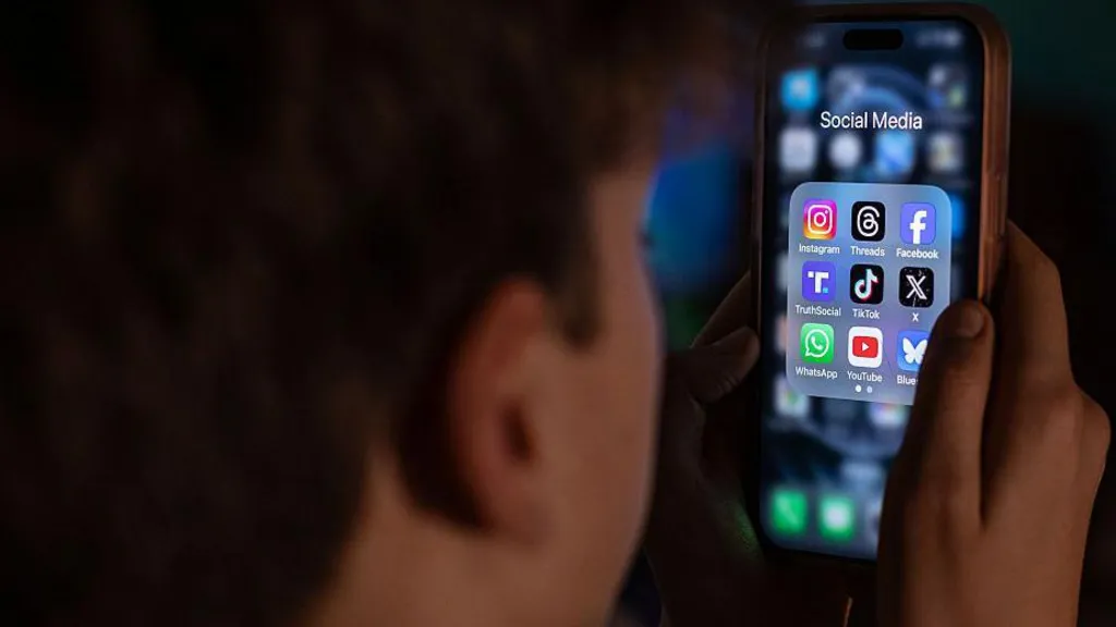 A boy looks at a smartphone screen displaying icons of apps that include Instagram, Threads, Facebook, TruthSocial, TikTok, X, WhatsApp, YouTube and Bluesky