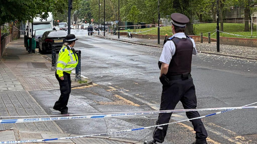 Two police officers stand by the side of a section of the road which has been cordoned off