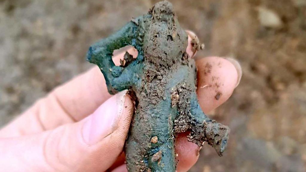 A hand holding the Cupid figurine covered in dirt