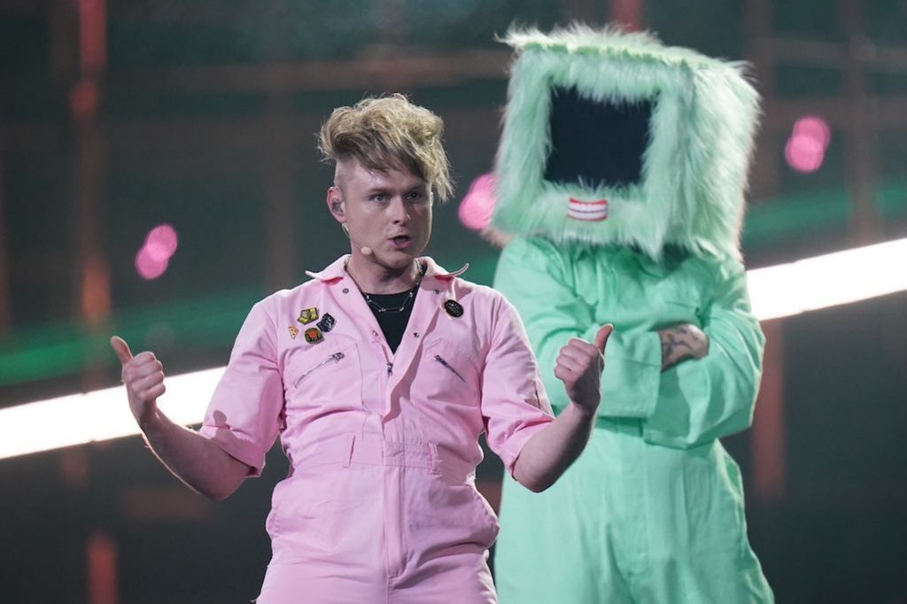Look Mum No Computer in a pink boiler suit with a dancer in a green one and a fluffy box on their head behind him